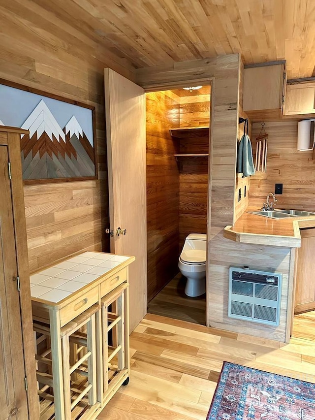 bathroom with a sink, toilet, wood ceiling, and wooden walls