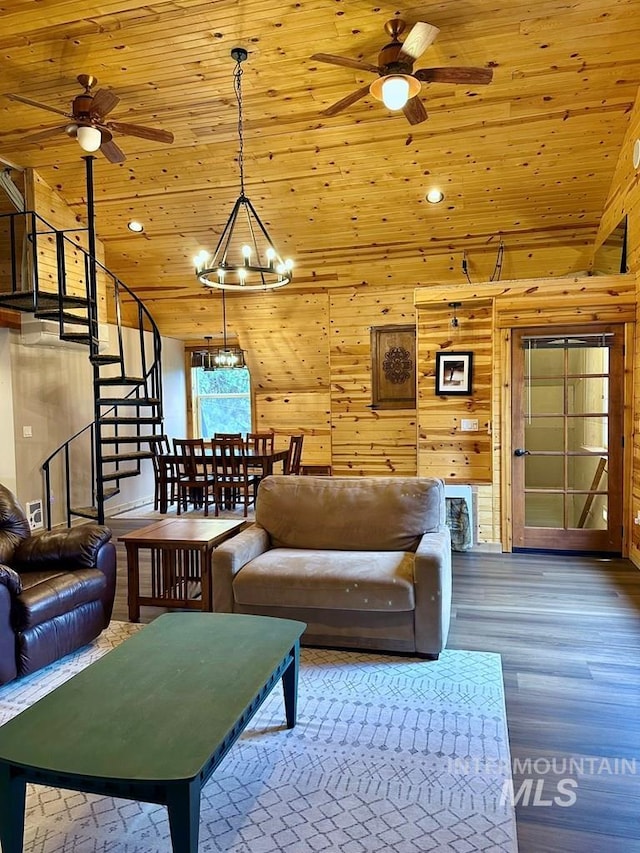 living area with stairway, wood walls, wood finished floors, and ceiling fan with notable chandelier