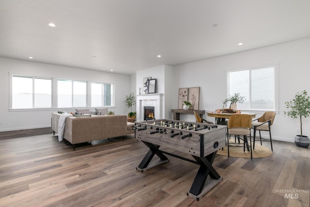 playroom featuring baseboards, a warm lit fireplace, wood finished floors, and recessed lighting