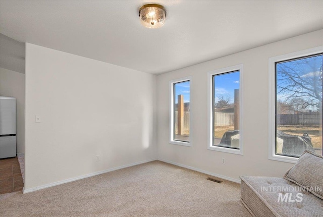 empty room featuring plenty of natural light, baseboards, visible vents, and light carpet