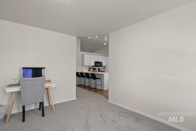 office featuring a textured ceiling, vaulted ceiling, baseboards, and light carpet