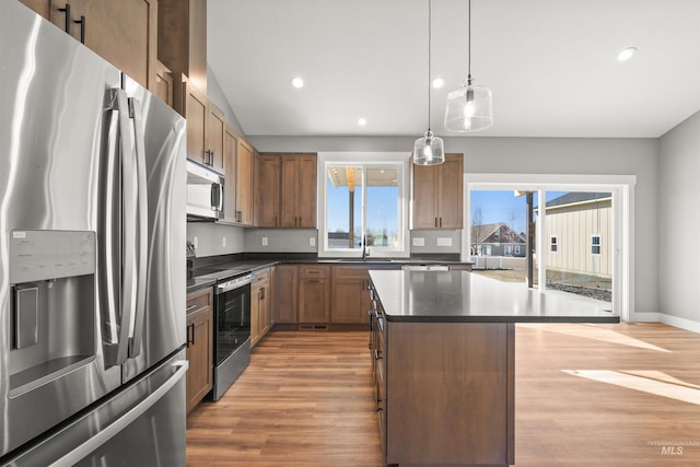 kitchen featuring dark countertops, a kitchen island, stainless steel appliances, light wood-type flooring, and a sink