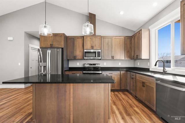 kitchen with a center island, decorative light fixtures, stainless steel appliances, a sink, and wood finished floors