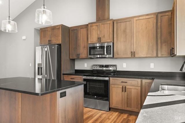 kitchen featuring dark countertops, appliances with stainless steel finishes, decorative light fixtures, light wood-style floors, and a sink