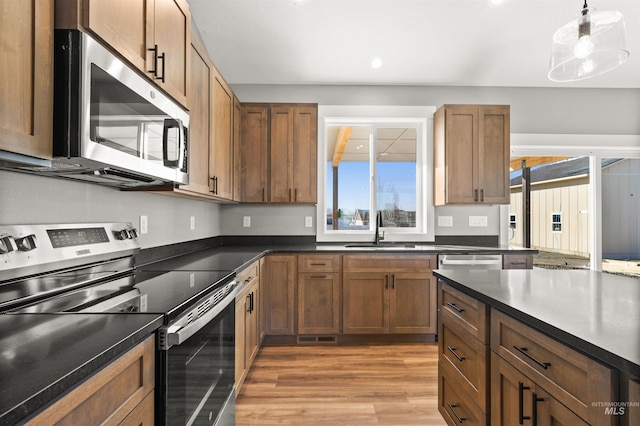 kitchen featuring dark countertops, light wood-style flooring, stainless steel appliances, and a sink