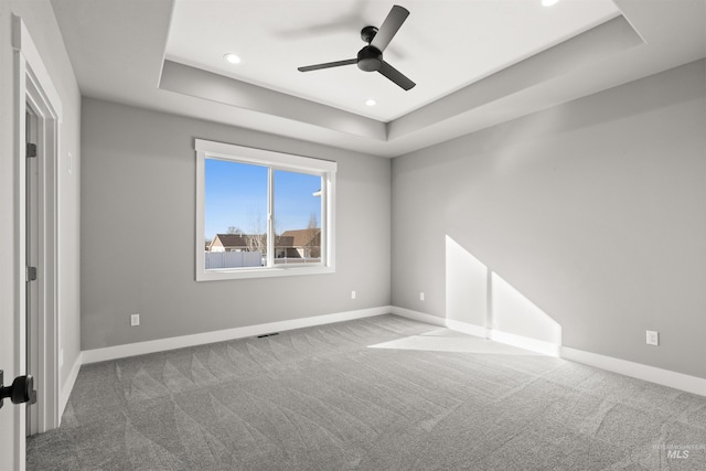 empty room featuring carpet floors, a raised ceiling, and baseboards