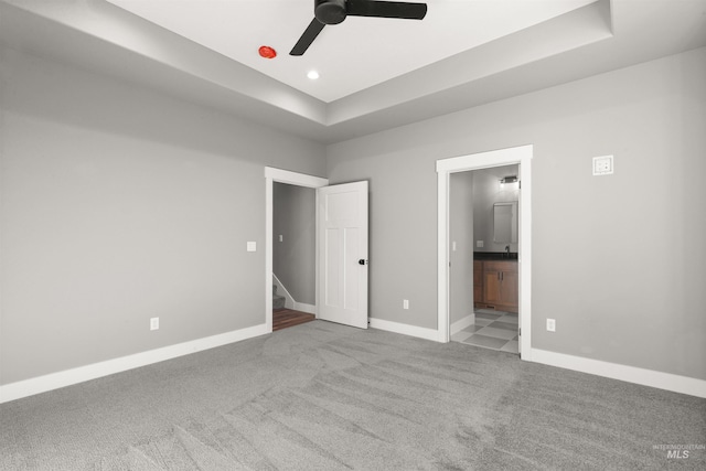 unfurnished bedroom with a tray ceiling, carpet flooring, baseboards, and ensuite bathroom