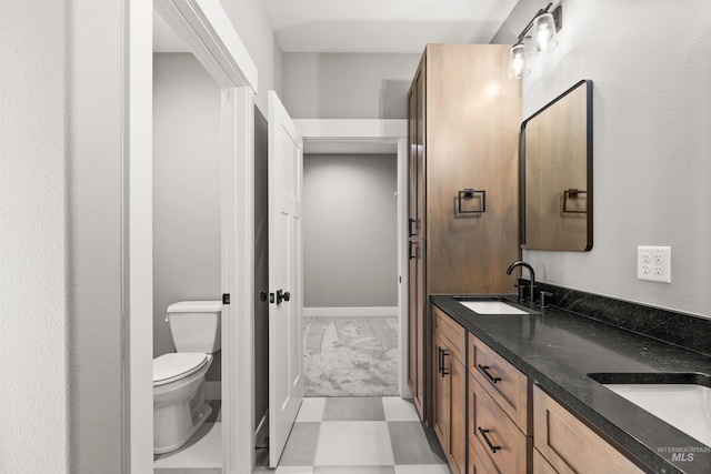 full bath with baseboards, a sink, toilet, and double vanity