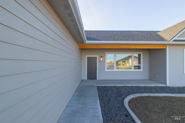 view of exterior entry featuring a shingled roof and a patio area