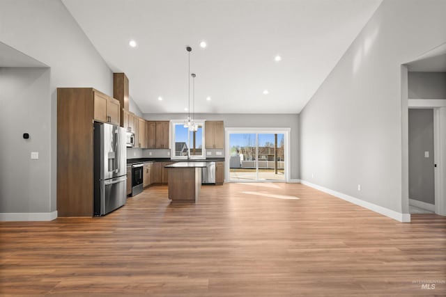 kitchen featuring light wood-style flooring, baseboards, open floor plan, appliances with stainless steel finishes, and dark countertops