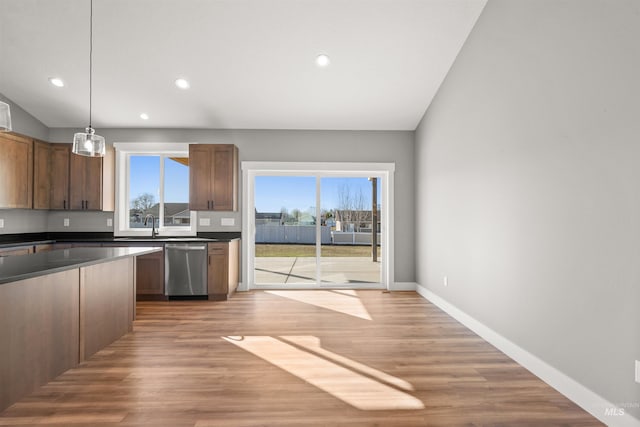 kitchen featuring light wood finished floors, baseboards, dark countertops, lofted ceiling, and stainless steel dishwasher