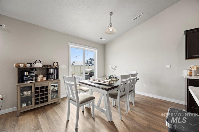 dining room with lofted ceiling, hardwood / wood-style floors, and a textured ceiling