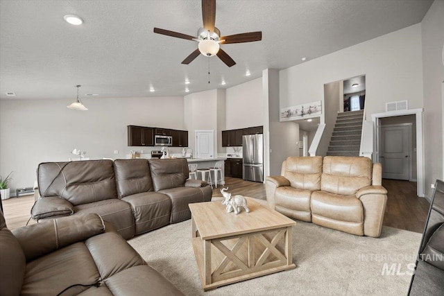 living room featuring ceiling fan, high vaulted ceiling, a textured ceiling, and light wood-type flooring