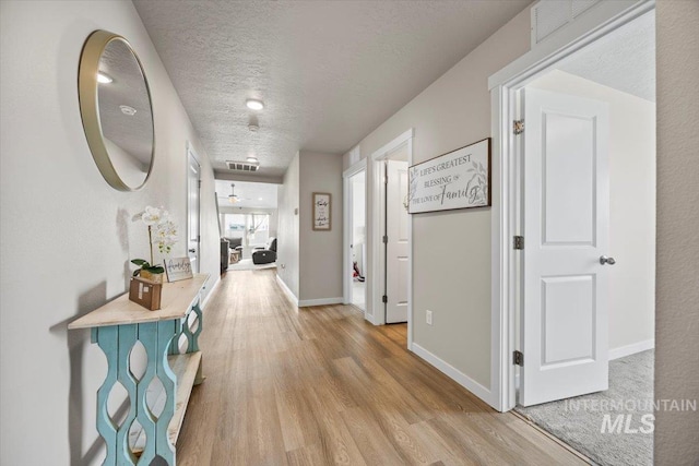 hallway with light hardwood / wood-style floors and a textured ceiling