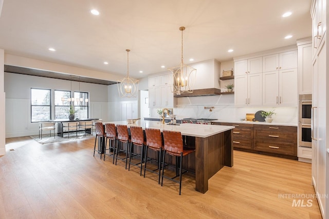 3426 N Hardwick Ave, Eagle, ID 83616 - kitchen featuring light wood-style floors, a decorative wall, white cabinetry, a center island with sink, and a breakfast bar