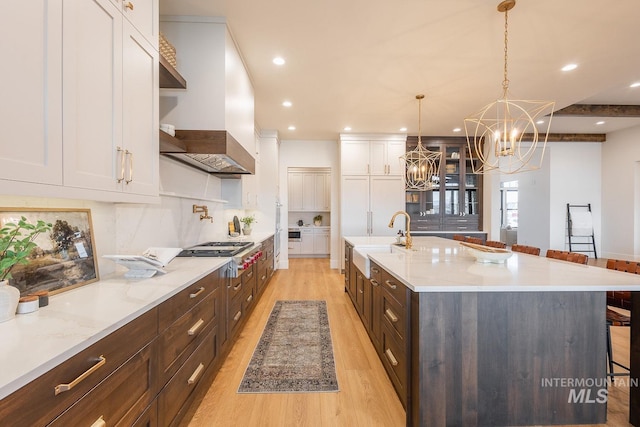 3426 N Hardwick Ave, Eagle, ID 83616 - kitchen with stainless steel gas stovetop, wall chimney range hood, white cabinetry, a chandelier, and light wood-type flooring