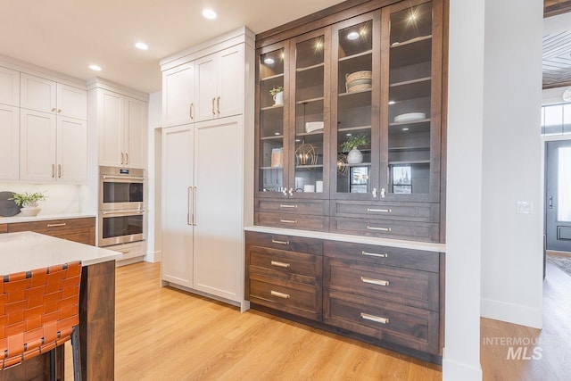 3426 N Hardwick Ave, Eagle, ID 83616 - kitchen with stainless steel double oven, light wood finished floors, glass insert cabinets, light countertops, and recessed lighting