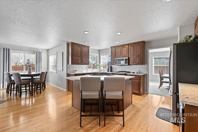 kitchen with light wood finished floors, decorative backsplash, light countertops, appliances with stainless steel finishes, and a kitchen breakfast bar