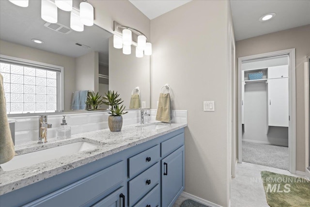 bathroom with a spacious closet, visible vents, double vanity, and a sink