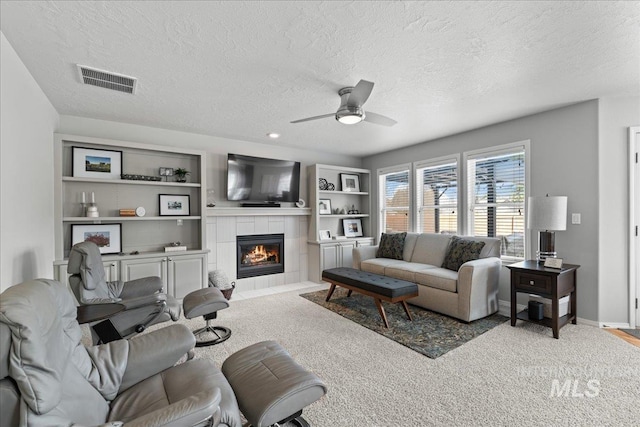 living room with visible vents, a ceiling fan, a textured ceiling, a fireplace, and baseboards