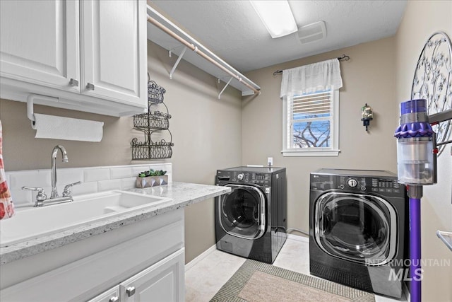 clothes washing area featuring light tile patterned floors, cabinet space, a sink, a textured ceiling, and washing machine and dryer