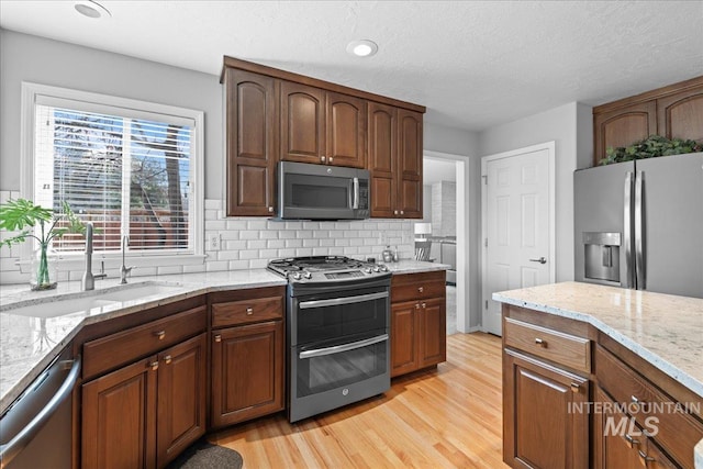 kitchen with light stone counters, a sink, appliances with stainless steel finishes, tasteful backsplash, and light wood-type flooring