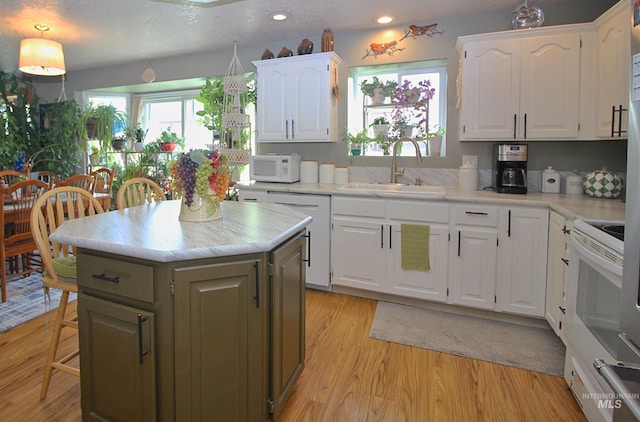 kitchen with white cabinetry, white appliances, light wood-style floors, and a sink