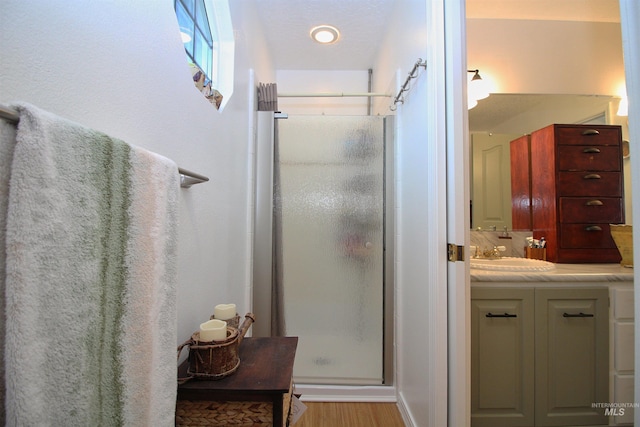 bathroom with wood finished floors, a shower stall, and vanity