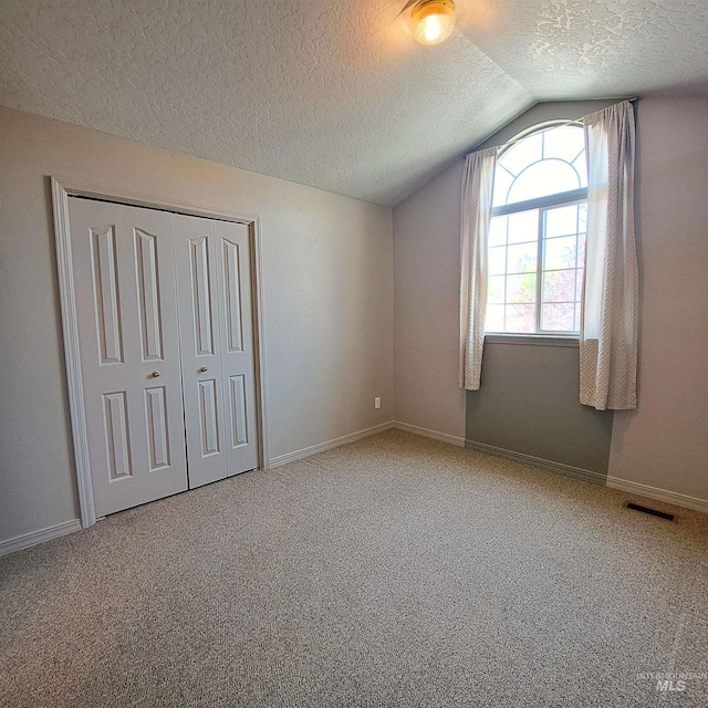 unfurnished bedroom featuring a textured ceiling, visible vents, vaulted ceiling, and carpet