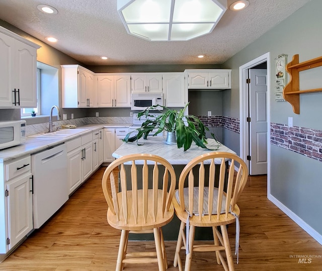 kitchen with white cabinets, white appliances, a textured ceiling, and a sink