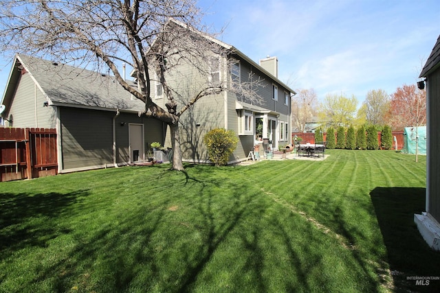 rear view of property with a chimney, a yard, a patio, and a fenced backyard