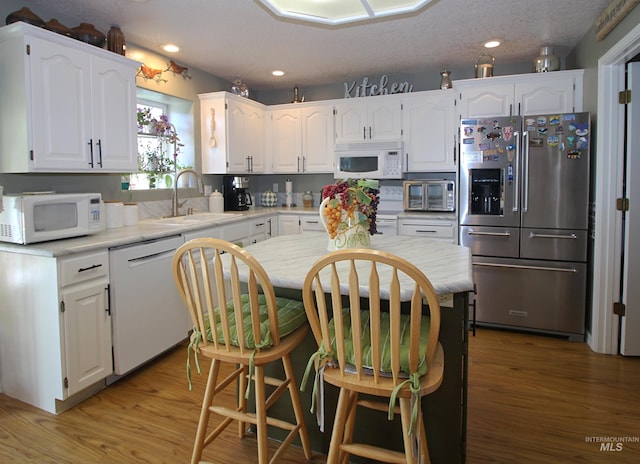 kitchen featuring white cabinetry, white appliances, light countertops, and a sink