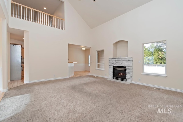 unfurnished living room with carpet floors, a stone fireplace, visible vents, and baseboards