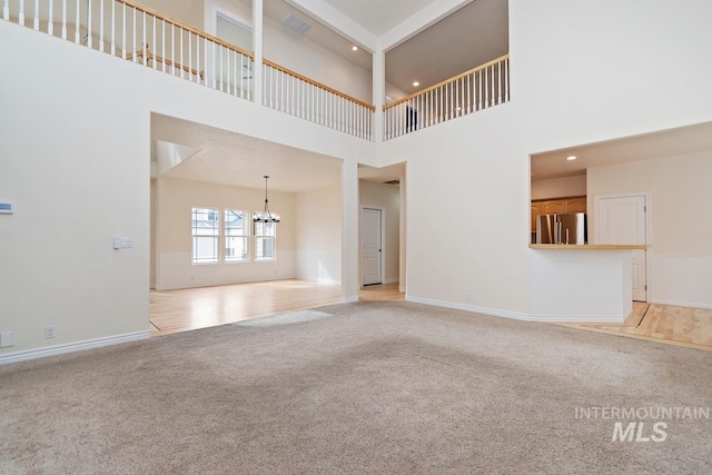 unfurnished living room with light carpet, a notable chandelier, a towering ceiling, and baseboards