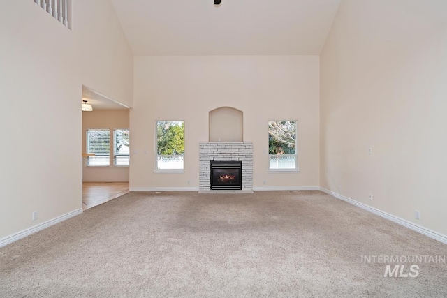 unfurnished living room featuring carpet, a high ceiling, baseboards, and a fireplace with flush hearth