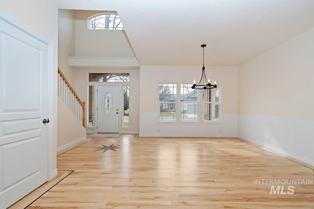 entrance foyer with light wood finished floors, stairs, a chandelier, and wainscoting