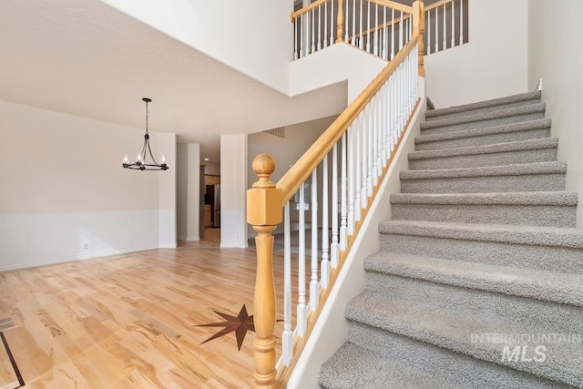 stairway featuring wainscoting, wood finished floors, a towering ceiling, and an inviting chandelier