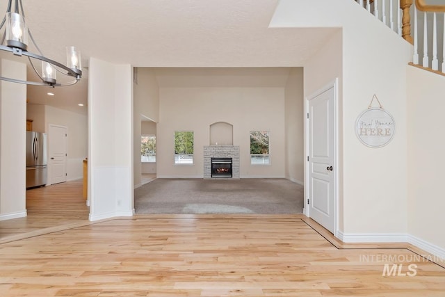 unfurnished living room with baseboards, a glass covered fireplace, wood finished floors, stairs, and a notable chandelier