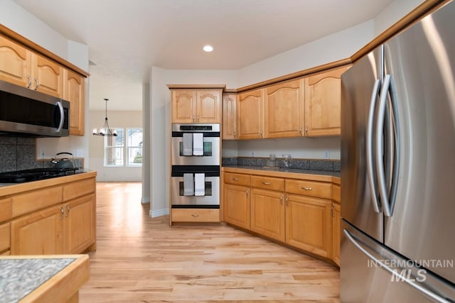 kitchen featuring decorative backsplash, appliances with stainless steel finishes, an inviting chandelier, light wood-type flooring, and recessed lighting