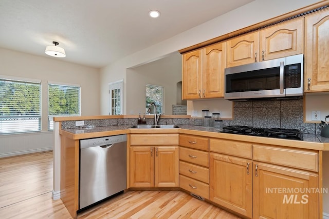 kitchen featuring a peninsula, a sink, stainless steel appliances, light wood-style floors, and backsplash