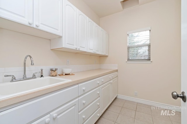 kitchen with light tile patterned flooring, a sink, white cabinetry, baseboards, and light countertops