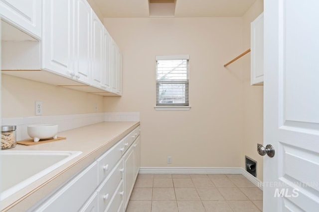 laundry room featuring cabinet space, a sink, baseboards, and light tile patterned flooring