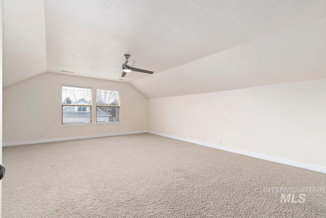 additional living space with light carpet, a textured ceiling, lofted ceiling, and baseboards