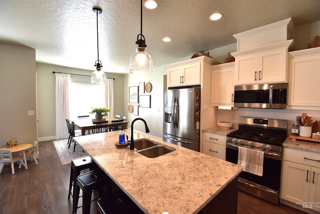 kitchen featuring a center island with sink, decorative backsplash, light stone counters, appliances with stainless steel finishes, and a sink