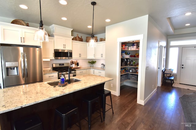 kitchen featuring decorative backsplash, light stone counters, a breakfast bar, appliances with stainless steel finishes, and dark wood-style flooring