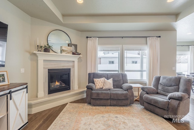 living area with recessed lighting, dark wood finished floors, a raised ceiling, and a glass covered fireplace