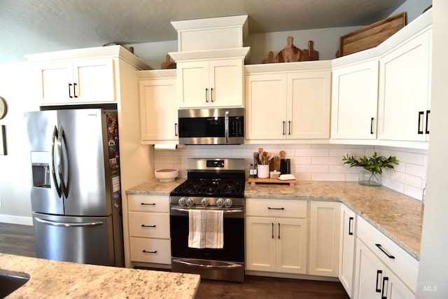 kitchen featuring stainless steel appliances, white cabinetry, backsplash, and light stone countertops