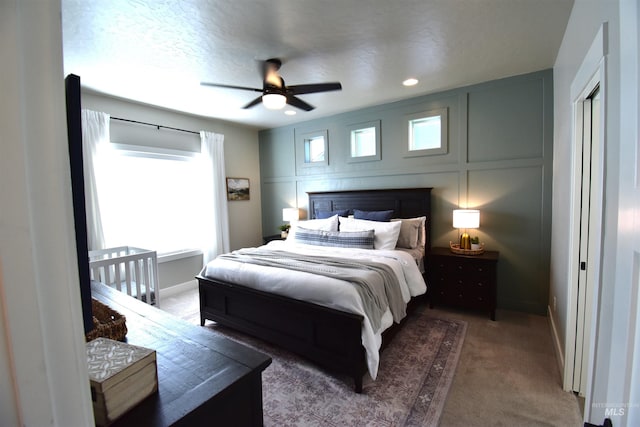 carpeted bedroom with a decorative wall, a textured ceiling, and ceiling fan