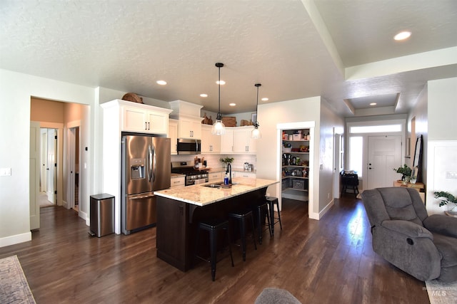 kitchen with dark wood-style flooring, a breakfast bar area, appliances with stainless steel finishes, open floor plan, and a sink