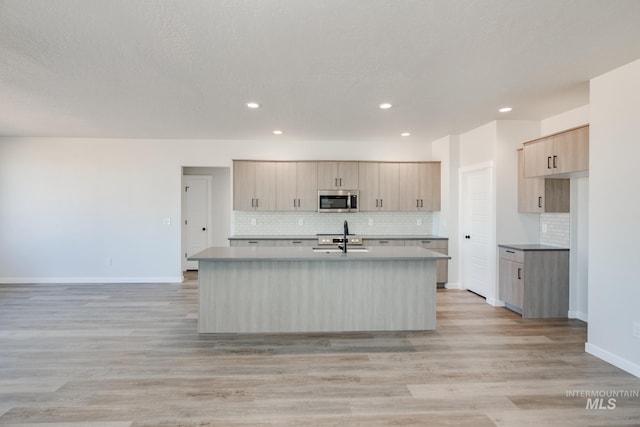8196 E Red Horse St, Nampa, ID 83687 - kitchen featuring stainless steel microwave, a kitchen island with sink, decorative backsplash, and light brown cabinets